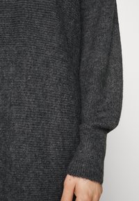 Mörkgrå texturerad tröja med ribbad design och lösa ärmar, tillverkad av mjukt tyg med en något fuzzy yta.