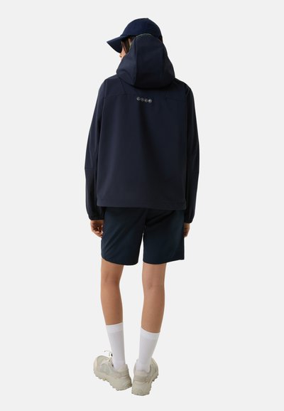 Navy hoodie with a drawstring hood, featuring a back logo detail. Paired with navy shorts and white socks, completed by light-colored sneakers.