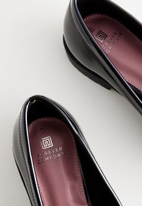 Chaussures en cuir verni noir avec un bout arrondi et un intérieur bordeaux. Présente le logo "Forever Comfort" sur la semelle intérieure.