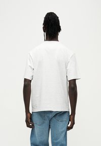 Γκρι βαμβακερό μπλουζάκι με χαλαρή εφαρμογή και κοντά μανίκια, που διαθέτει απλό σχέδιο και στρογγυλή γραμμή στο ντεκολτέ. Φορεμένο με μπλε τζιν.