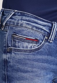 Valkoiset denim-farkut, joissa on klassinen viiden taskun muotoilu. Sisältää pienen takataskun, jossa on punavalko-siniratkaisu.