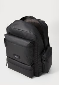 Black backpack made of smooth, durable material. Features multiple zippered pockets, including a front pocket and side pouch.