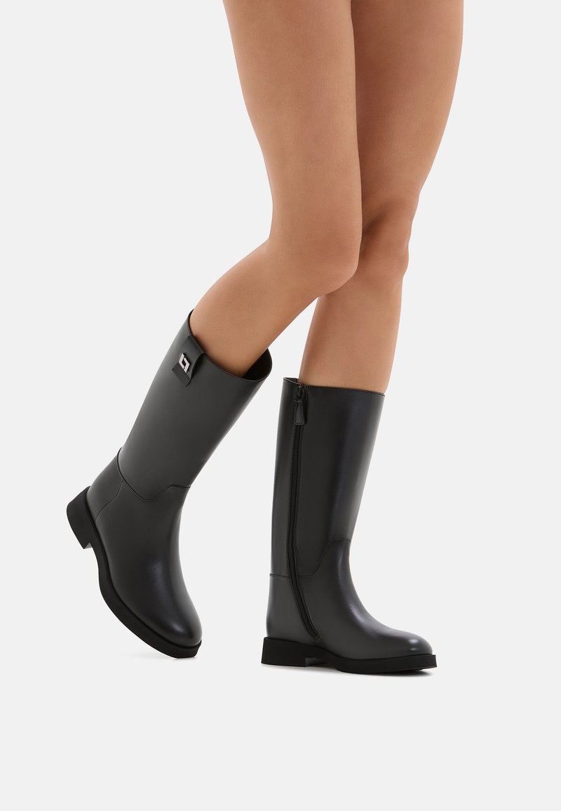 Stivali neri in gomma alti fino al ginocchio con una superficie liscia, punta tondeggiante e zip laterale. Presenta un piccolo logo sul sopracchio.