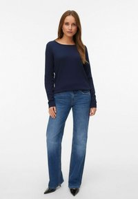 Top blu navy a maniche lunghe con un motivo texturizzato, abbinato a jeans azzurri a gamba dritta e tacchi neri a punta.