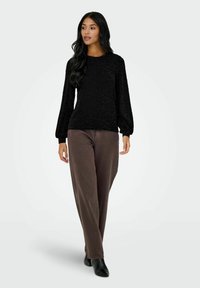 Svart teksturert langermet topp med rund hals, kombinert med brune vidbukser og svarte ankelstøvler. Enkel, avslappet antrekk.