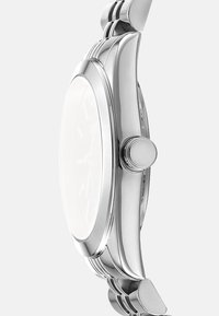 Orologio in metallo argento con finitura lucida, cassa rotonda, quadrante minimalista e cinturino texturizzato con maglie curve e una corona lateralmente.