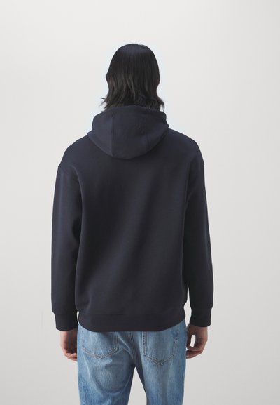 Felpa navy con un grande cappuccio morbido, maniche lunghe e polsini a coste, abbinata a jeans in denim azzurro chiaro. Tessuto liscio.