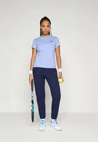 Lys blå kortermet t-skjorte med logo, kombinert med marineblå bukser. Tilbehør inkluderer et tennisslag og en gul tennisball.