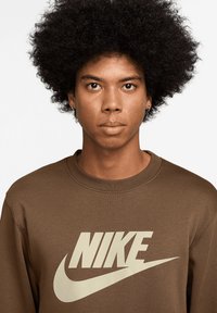 Felpa marrone con logo Nike color beige chiaro. Girocollo e polsini a costine. Il tessuto sembra morbido con una texture liscia.