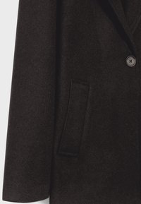 Gros plan sur un manteau en laine brun foncé montrant un bouton, un revers, une manche et une poche passepoilée verticale.