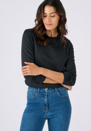 Zwart shirt met lange mouwen en een ronde halslijn, zachte textuur en aangesloten manchetten, gecombineerd met hooggetailleerde blauwe spijkerbroek.
