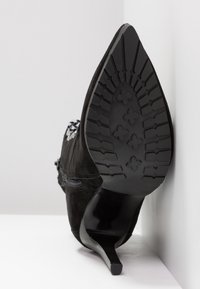 Black suede ankle boot with a pointed toe and a slim heel. The textured sole features a patterned grip. Side zipper detail visible.