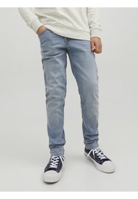 Světlé modré džíny s úzkým střihem, spárované s námořnickými teniskami s bílými šňůrkami a gumovými podrážkami. Šedý, strukturovaný svetr s dlouhým rukávem.