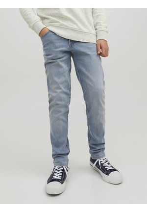 Jeans en denim bleu clair à coupe slim, associés à des baskets bleu marine avec des lacets blancs et des semelles en caoutchouc. Haut long à manches longues gris texturé.