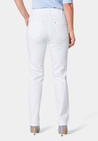 Weißes Denim-Jeans mit schmaler Passform, ausgestattet mit zwei Gesäßtaschen und minimalem Zubehör. Glatte Textur, gerades Bein-Design und knöchellang.