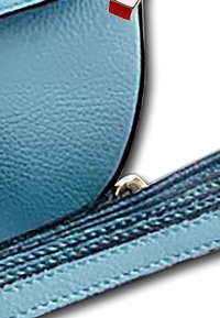 Blauwe textuur leren tas met zwarte randen, voorzien van een zilveren rits en een klein rood accentkaartje. Close-up van het ritsgebied.