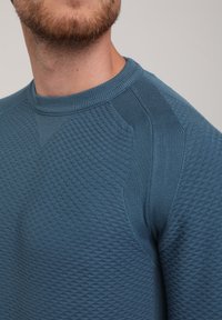 Maglione blu testurizzato con scollo rotondo, caratterizzato da un motivo a righe diagonali e orizzontali sulle spalle e sul corpo.