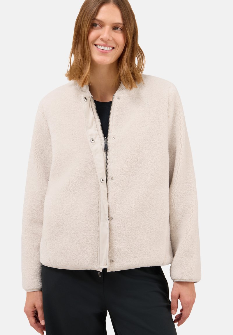 Veste en polaire beige clair avec une doublure intérieure lisse, des boutons-pression et une coupe décontractée. Texture douce et longues manches sans motifs visibles.