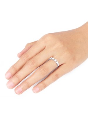 Main avec un teint de peau moyen portant une bague en argent en forme d'étoiles reliées au doigt annulaire, sur fond blanc.