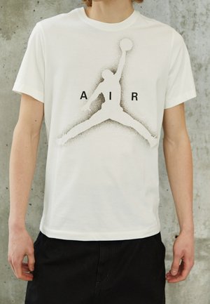 Person trägt ein weißes T-Shirt mit einer schwarzen Silhouette eines Basketballspielers, der springt und einen Ball hält, mit den Buchstaben A I R um die Figur herum.