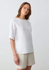 Witte linnen korte mouwen blouse met een ronde halslijn en een ontspannen pasvorm, gecombineerd met beige linnen shorts. Soepele textuur en eenvoudig ontwerp.