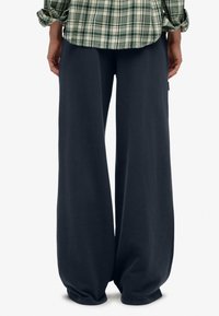 Donkergrijze wijde sweatpants hebben een zachte textuur en elastische boorden. Gecombineerd met een groen geruit shirt heeft de outfit een relaxte pasvorm.