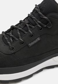 Black hiking shoe with a suede and textile upper, contrasting white midsole, textured rubber outsole, and reflective laces, featuring a logo.