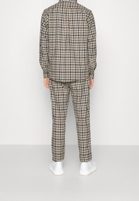 Rutiga skjortor och byxor i brunt, svart och vitt, med långa ärmar och elastiska muddar. Vita skor fulländar outfiten.