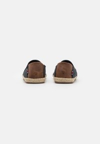 Sorte tekstil slip-on sko med brune skinnakenter og en vevd jute såle. Fleksibel design, avrundet tå og minimale sømdetaljer.