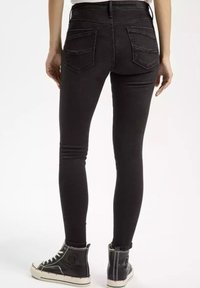 Czarne wąskie dżinsy z tylnymi kieszeniami, slim-fit, z lekkim stretch'em, w połączeniu z czarnymi sneakersami za kostkę.