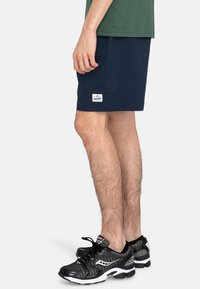 Navy cotton shorts feature a straight cut and a small white logo patch. Black mesh running shoes with white accents complete the outfit.