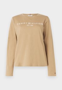 Beige Langarm-T-Shirt aus Baumwolle mit einem weißen Drucklogo "TOMMY HILFIGER" und "EST. 1985" auf der Vorderseite, mit Rundhalsausschnitt.