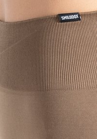 Ceinture marron côtelée de bas d'habillement de sport avec une surface texturée. Comprend une étiquette noire portant la marque "SMILODOX".