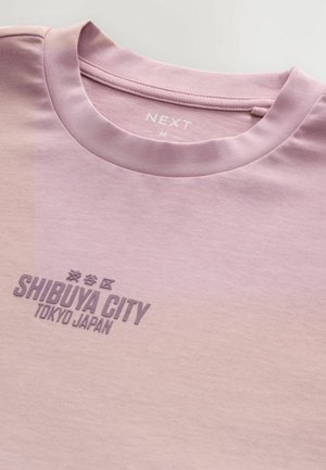 Ljusrosa bomulls-t-shirt med rund halsringning, med texten "SHIBUYA CITY TOKYO JAPAN" i mörkare lila; slät textur och minimalistisk design.