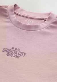 Lyserød bomulds T-shirt med rund hals, der har et grafisk print, som lyder "SHIBUYA CITY TOKYO JAPAN" i mørkegrå.