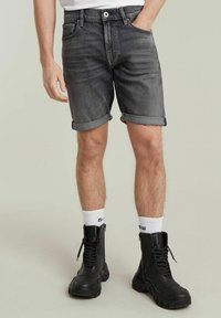 Grijze denim shorts met opgerolde zomen, voorzien van een knoopsluiting aan de voorkant en vijf zakken, gecombineerd met zwarte veterschoenen en witte sokken.