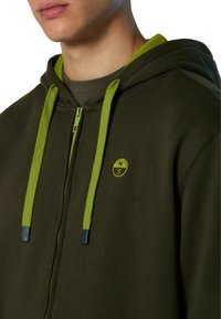 Hoodie verde oliva con zip sul fronte, lacci a contrasto di verde lime e un logo rotondo. Realizzato in tessuto morbido con una texture liscia.