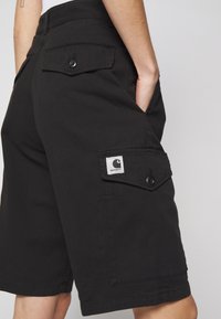 Des shorts cargo noirs en tissu résistant, dotés de plusieurs poches, de fermetures à bouton et d'un petit logo cousu sur le côté.