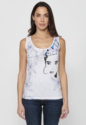 Débardeur blanc sans manches avec un motif floral et une impression graphique de visage en accents noir et bleu. Le tissu est lisse et léger.