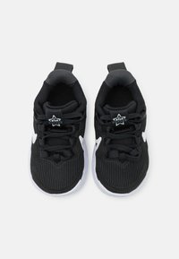 Chaussures de sport noires avec une tige en maille texturée, des accents de logo blancs et une semelle en caoutchouc. Équipées de lacets et d'un col rembourré pour le confort.