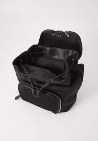 Black nylon backpack with a drawstring closure, zippered front pocket, and smooth texture. Features silver hardware and an inner pocket.