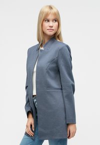 Sivý šitý blejzer s okrúhlym golierom, bočnými vreckami a štruktúrovanými ramenami. Vyrobený z textúrovaného materiálu, má rovný strih.