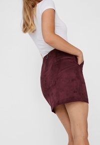 Marlowe Minirock aus burgunderfarbenem Wildleder mit glatter Textur, ausgestattet mit einer seitlichen Reißverschlusstasche und einem leicht geschwungenen Saum.