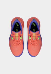 Φωτεινά αθλητικά παπούτσια κοραλλί με διάτρητο επάνω μέρος, μοβ λεπτομέρειες και πράσινα μεταλλικά στοιχεία. Διαθέτουν επίπεδα κορδόνια και επενδεδυμένο γιακά για άνεση.