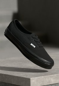 Zwarte canvas sneaker met gestructureerde bovenkant, ronde neus, platte veters en rubberen zool. Heeft een subtiele logotag aan de zijkant.