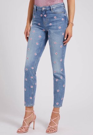 Jasnoniebieskie dżinsy z małymi różowymi wzorami kwiatów, noszone z różowymi sandałami na obcasie i błyszczącym różowym topem.