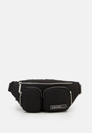 Sac banane noir Calvin Klein avec trois compartiments zippés, dont deux poches avant, et une sangle ajustable.