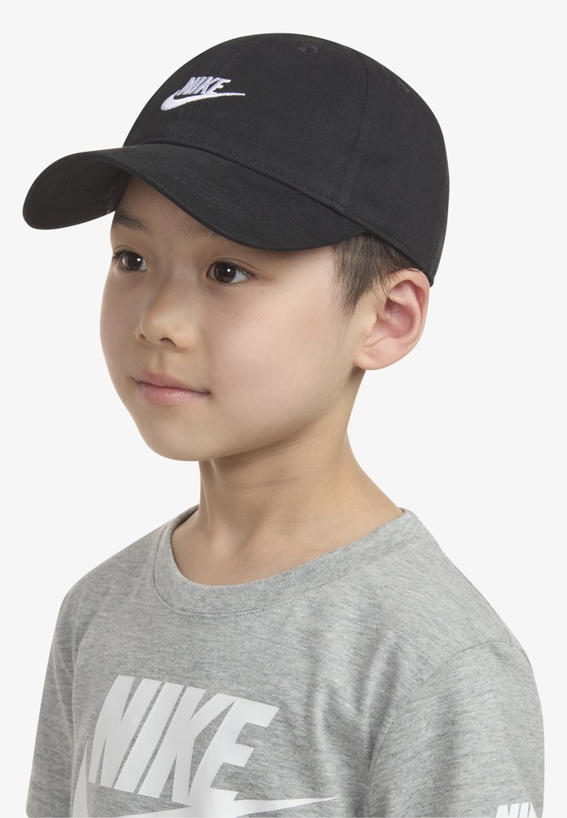 Μαύρο καπέλο του μπέιζμπολ με καμπύλο γείσο, διακοσμημένο με λευκό κεντημένο λογότυπο Nike. Φορεμένο με γκρι μπλουζάκι που εμφανίζει ένα μεγάλο λευκό λογότυπο.