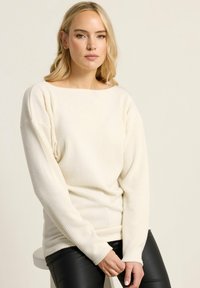 Cremefarbener, gerippter Pullover mit weitem Ausschnitt und langen Ärmeln, kombiniert mit schwarzen Lederhosen, die einen lockeren Sitz und eine weiche Textur aufweisen.