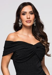 Schwarzes Kleid mit Carmenausschnitt aus strukturierter, funkelnder Stoff. Verfügt über ein verdrehtes Design an der Brust und florale Ohrringe mit Strasssteinen.